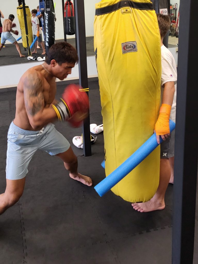 Student working the heavy bag while class continues behind him.